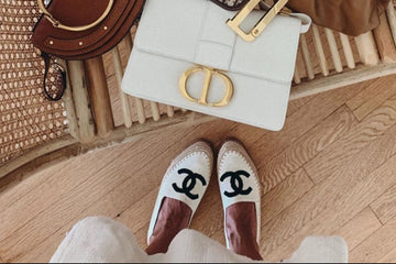 Three handbags including a white Dior bag, a brown textured bag, and a brown leather bag on a wooden floor.